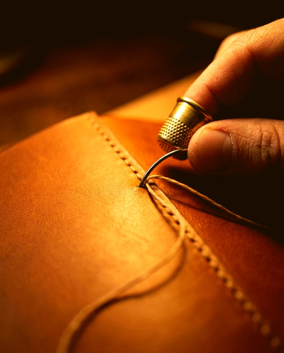 Close macro of saddle stitching through full-grain leather in warm workshop light